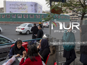 A group of young Iranian women, some of whom are not wearing mandatory headscarves, sit and stand at an outdoor fast-food restaurant in down...