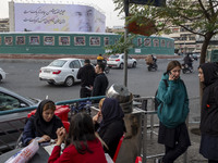 A group of young Iranian women, some of whom are not wearing mandatory headscarves, sit and stand at an outdoor fast-food restaurant in down...