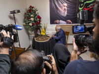 Former Iranian Foreign Minister, Mohammad Javad Zarif, signs a memorial notebook while sitting under a portrait of Lebanon's Hezbollah Secre...