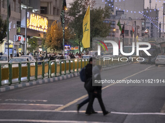 Iranian youths walk under a flag of Lebanon's Hezbollah that hangs on an avenue to commemorate Hezbollah Secretary General Hassan Nasrallah,...