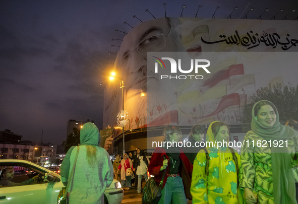 A group of young Iranian women, some of whom do not wear mandatory headscarves, walk under a giant banner featuring a portrait of Lebanon's...