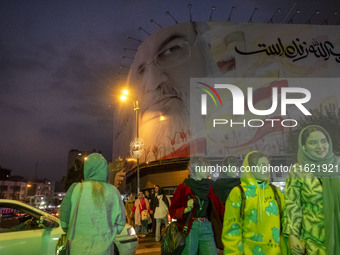 A group of young Iranian women, some of whom do not wear mandatory headscarves, walk under a giant banner featuring a portrait of Lebanon's...