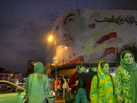 A group of young Iranian women, some of whom do not wear mandatory headscarves, walk under a giant banner featuring a portrait of Lebanon's...