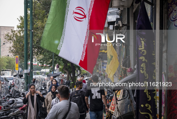 Iranian people walk past an Iranian flag and a flag of Lebanon's Hezbollah, displayed on a sidewalk to commemorate Hezbollah Secretary Gener...