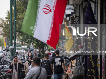 Iranian people walk past an Iranian flag and a flag of Lebanon's Hezbollah, displayed on a sidewalk to commemorate Hezbollah Secretary Gener...