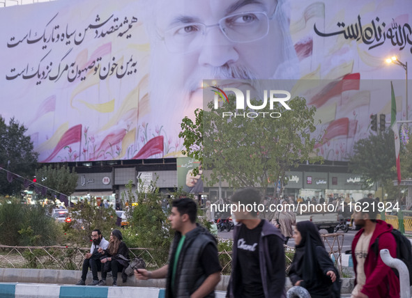 Iranian youths walk under a giant banner featuring a portrait of Lebanon's Hezbollah Secretary General, Hassan Nasrallah, in downtown Tehran...