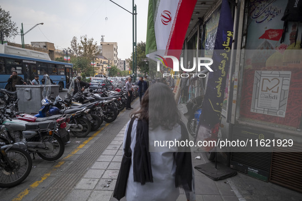 A young Iranian woman, who does not wear a mandatory headscarf, walks under an Iranian flag displayed on a sidewalk to commemorate Hezbollah...