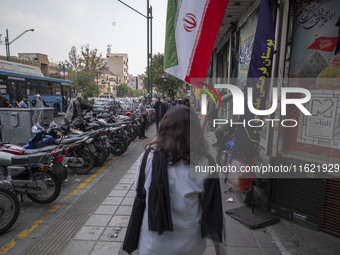 A young Iranian woman, who does not wear a mandatory headscarf, walks under an Iranian flag displayed on a sidewalk to commemorate Hezbollah...