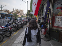 A young Iranian woman, who does not wear a mandatory headscarf, walks under an Iranian flag displayed on a sidewalk to commemorate Hezbollah...