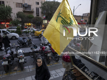 An Iranian woman walks under a Hezbollah flag displayed on a sidewalk to commemorate Hezbollah Secretary General Hassan Nasrallah, who was k...