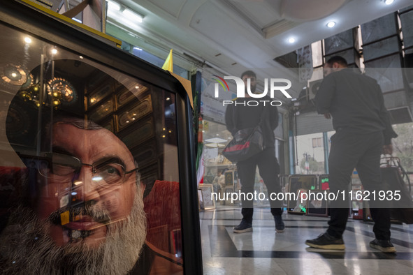 Two men stand next to a framed portrait of Lebanon's Hezbollah Secretary General, Hassan Nasrallah, who was killed in an Israeli air strike...