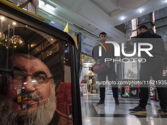 Two men stand next to a framed portrait of Lebanon's Hezbollah Secretary General, Hassan Nasrallah, who was killed in an Israeli air strike...