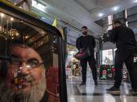 Two men stand next to a framed portrait of Lebanon's Hezbollah Secretary General, Hassan Nasrallah, who was killed in an Israeli air strike...