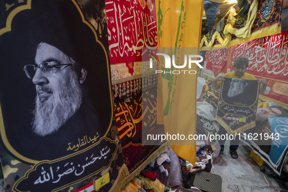 An Iranian trader holds a flag featuring a portrait of Lebanon's Hezbollah Secretary General, Hassan Nasrallah, for his client (not pictured...