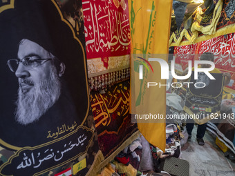 An Iranian trader holds a flag featuring a portrait of Lebanon's Hezbollah Secretary General, Hassan Nasrallah, for his client (not pictured...