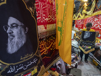 An Iranian trader holds a flag featuring a portrait of Lebanon's Hezbollah Secretary General, Hassan Nasrallah, for his client (not pictured...