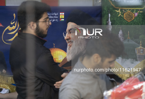 Two Iranian men stand in front of a portrait of Lebanon's Hezbollah Secretary General, Hassan Nasrallah, who was killed in an Israeli air st...