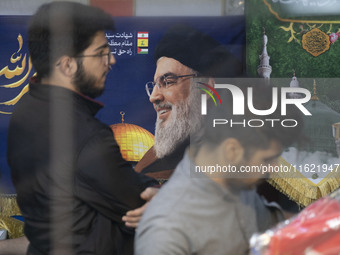 Two Iranian men stand in front of a portrait of Lebanon's Hezbollah Secretary General, Hassan Nasrallah, who was killed in an Israeli air st...