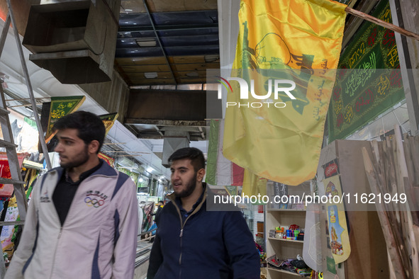 Two young Iranian men walk under a flag of Lebanon's Hezbollah while shopping at a war toys and religious accessory shopping mall in downtow...