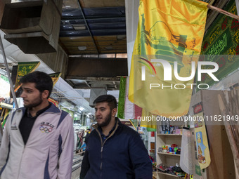 Two young Iranian men walk under a flag of Lebanon's Hezbollah while shopping at a war toys and religious accessory shopping mall in downtow...