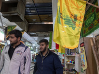 Two young Iranian men walk under a flag of Lebanon's Hezbollah while shopping at a war toys and religious accessory shopping mall in downtow...