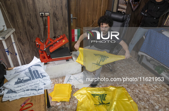 An Iranian worker holds a printed flag of Lebanon's Hezbollah at a flag and banner printing workshop at a war toys and religious accessory s...