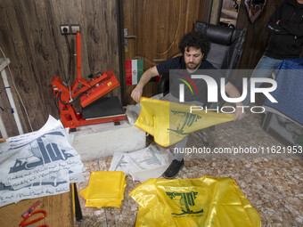 An Iranian worker holds a printed flag of Lebanon's Hezbollah at a flag and banner printing workshop at a war toys and religious accessory s...