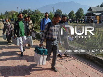 Polling officials carry electronic voting machines (EVM) at a distribution center in Sumbal area of Bandipora district, North of Srinagar, o...