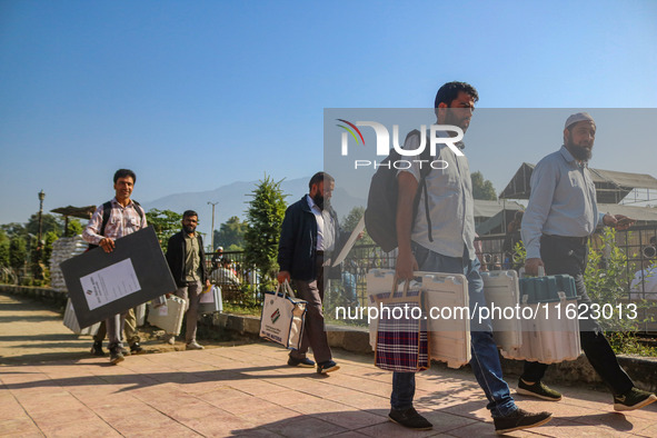 Polling officials carry electronic voting machines (EVM) at a distribution center in Sumbal area of Bandipora district, North of Srinagar, o...