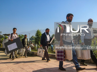 Polling officials carry electronic voting machines (EVM) at a distribution center in Sumbal area of Bandipora district, North of Srinagar, o...