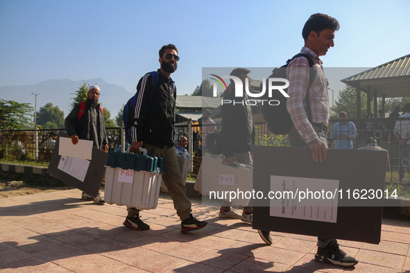 Polling officials carry electronic voting machines (EVM) at a distribution center in Sumbal area of Bandipora district, North of Srinagar, o...