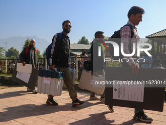 Polling officials carry electronic voting machines (EVM) at a distribution center in Sumbal area of Bandipora district, North of Srinagar, o...