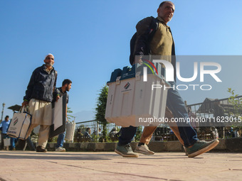 Polling officials carry electronic voting machines (EVM) at a distribution center in Sumbal area of Bandipora district, North of Srinagar, o...