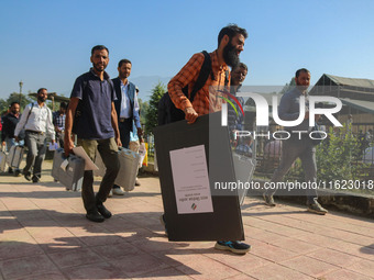 Polling officials carry electronic voting machines (EVM) at a distribution center in Sumbal area of Bandipora district, North of Srinagar, o...