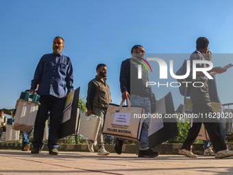 Polling officials carry electronic voting machines (EVM) at a distribution center in Sumbal area of Bandipora district, North of Srinagar, o...