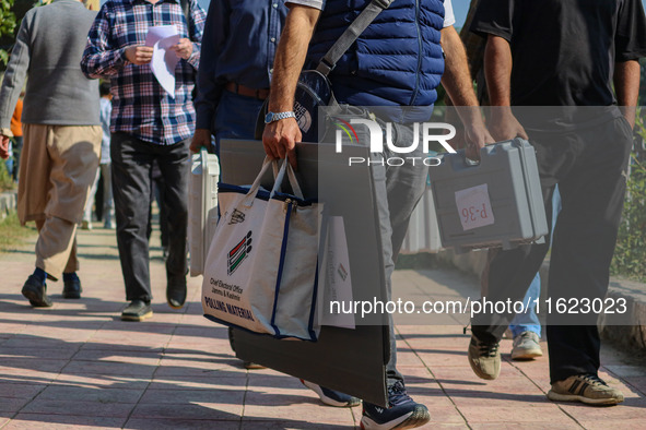 Polling officials carry electronic voting machines (EVM) at a distribution center in Sumbal area of Bandipora district, North of Srinagar, o...