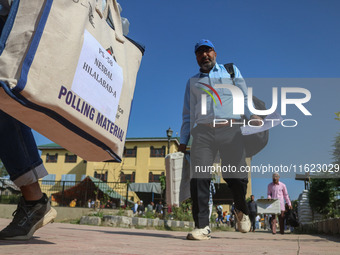 Polling officials carry electronic voting machines (EVM) at a distribution center in Sumbal area of Bandipora district, North of Srinagar, o...