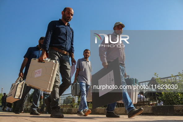 Polling officials carry electronic voting machines (EVM) at a distribution center in Sumbal area of Bandipora district, North of Srinagar, o...