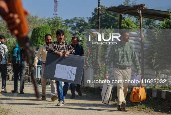 An Indian paramilitary soldier stands guard as polling officials carry electronic voting machines (EVM) at a distribution center in the Sumb...