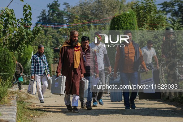 Polling officials carry electronic voting machines (EVM) at a distribution center in Sumbal area of Bandipora district, North of Srinagar, o...