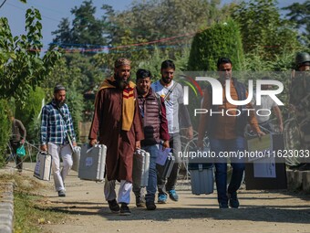 Polling officials carry electronic voting machines (EVM) at a distribution center in Sumbal area of Bandipora district, North of Srinagar, o...