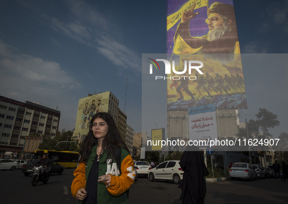 A young Iranian woman who does not wear a mandatory headscarf walks under a giant banner featuring a portrait of Lebanon's Hezbollah Secreta...