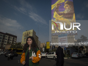 A young Iranian woman who does not wear a mandatory headscarf walks under a giant banner featuring a portrait of Lebanon's Hezbollah Secreta...