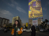 A young Iranian woman who does not wear a mandatory headscarf walks under a giant banner featuring a portrait of Lebanon's Hezbollah Secreta...