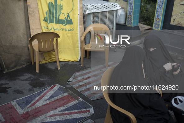 Two veiled Iranian women sit together in front of the U.S. flag, a British flag, and a flag of Lebanon's Hezbollah during a protest gatherin...