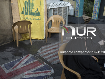 Two veiled Iranian women sit together in front of the U.S. flag, a British flag, and a flag of Lebanon's Hezbollah during a protest gatherin...