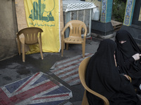 Two veiled Iranian women sit together in front of the U.S. flag, a British flag, and a flag of Lebanon's Hezbollah during a protest gatherin...