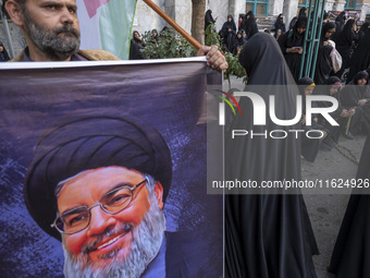 An Iranian protester holds a banner featuring a portrait of Lebanon's Hezbollah Secretary General, Hassan Nasrallah, while taking part in a...