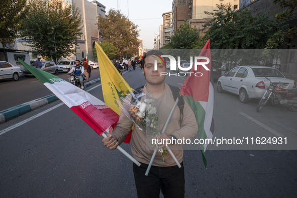 An Iranian protester carries an Iranian flag, a Palestinian flag, a flag of Lebanon's Hezbollah, and flowers while taking part in a protest...