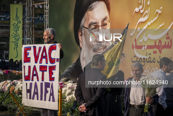 An elderly Iranian protester holds an anti-Israeli placard while standing in front of a giant banner depicting a portrait of Lebanon's Hezbo...